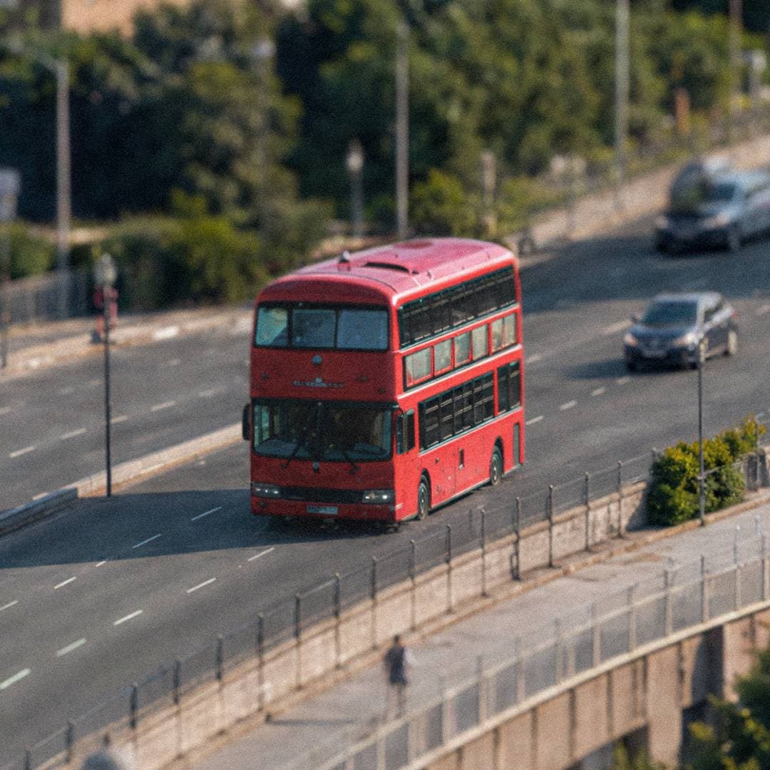 A classic red double-decker bus drives through a football-themed city area.