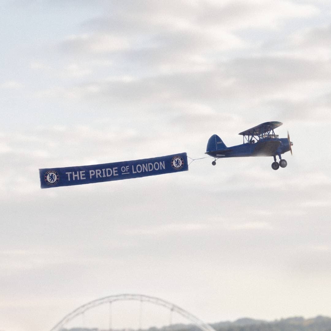 A vintage plane tows a football club banner over a bright urban skyline.