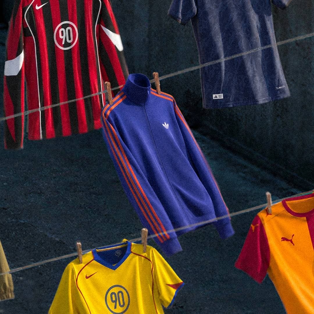 Classic football shirts and a blue adidas-style jacket hang on clotheslines between buildings.